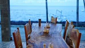A wooden dining table with chairs, set up outdoors with a view of the ocean. - Bali Apnea Club - Hostel (Kubu)