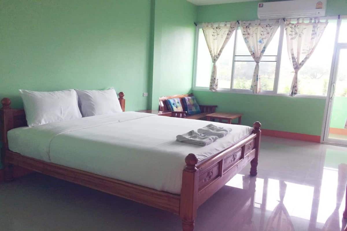 Una habitación con cama, mesita de noche, ventana con cortinas y equipo de aire acondicionado.