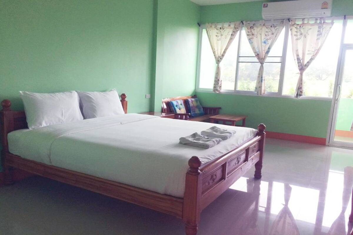 Un dormitorio con cama de madera, paredes verdes y una ventana con cortinas.