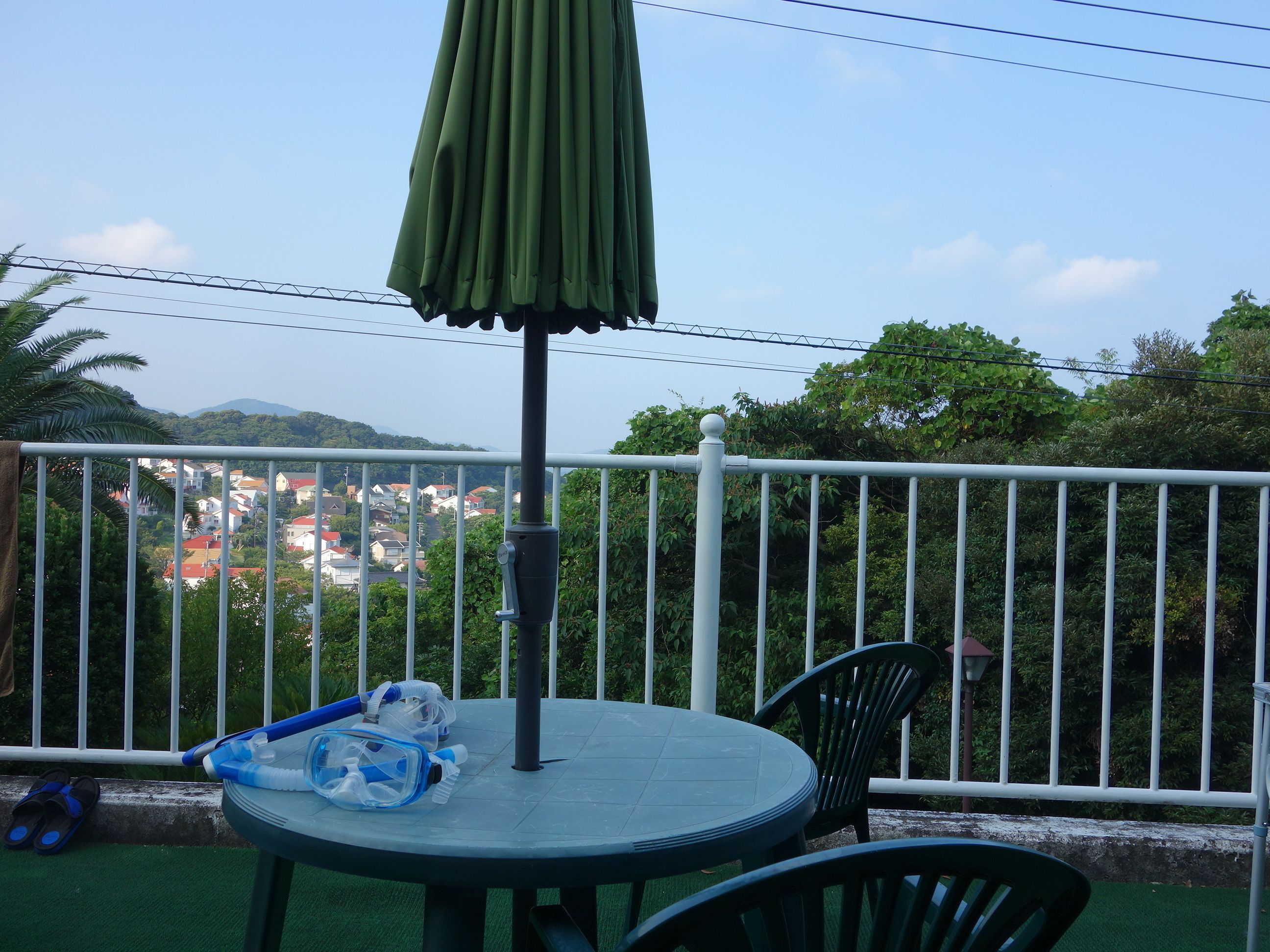 A balcony with a round table, a green umbrella, and a pair of blue snorkeling gear.