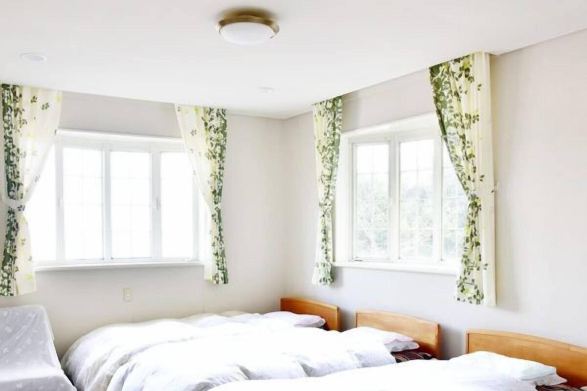 Une chambre avec deux lits, une chaise et de grandes fenêtres ornées de rideaux à motifs floraux.