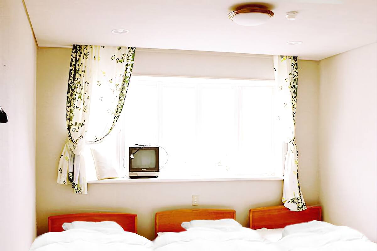 Une chambre à coucher avec un lit, une fenêtre avec des rideaux et un téléviseur posé sur une petite table.