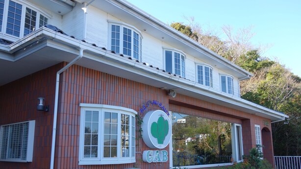 A two-story building with a restaurant sign, large windows, and a covered outdoor seating area. - Goishigahama House (Shimoda)