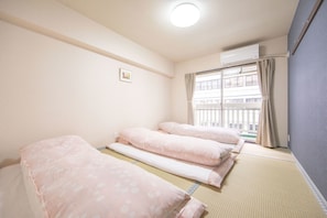 A room with three beds arranged in a row, a window with curtains, and an air conditioning unit on the wall. - Minhouses (Kyoto)