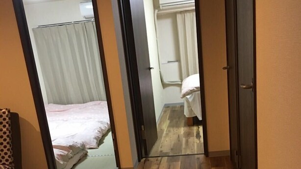 A narrow hallway with wooden flooring leading to a bedroom with a bed and a bathroom with a shower. - Minhouses (Kyoto)