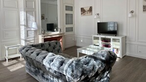 Una sala de estar con un sofá capitonado, un televisor de pantalla plana sobre un mueble blanco y una chimenea.