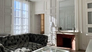 A living room with a dark velvet sofa, a glass coffee table, and a fireplace. - Hotel Particulier de Champrond (Chartres)
