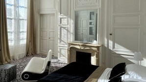 Una habitación de hotel con una cama, una silla, una chimenea y un espejo grande.