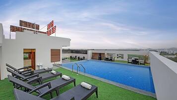 A rooftop pool with lounge chairs and a view of the city.