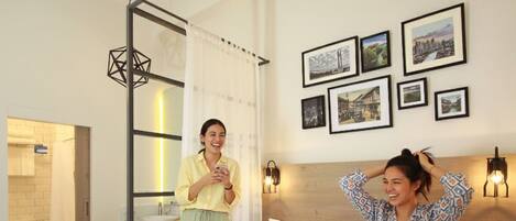 A hotel room with a bed, a bathroom with a toilet and sink, a hanging light fixture, and framed pictures on the wall.