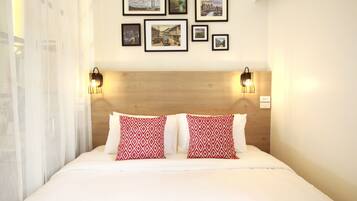A hotel room with a wooden headboard, two red patterned pillows, a white bedspread, and several framed pictures on the wall.