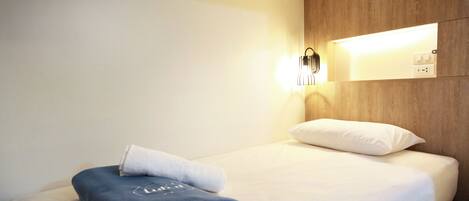 A neatly made bed with a folded towel and a pillow, a wall-mounted light, and a wooden panel.