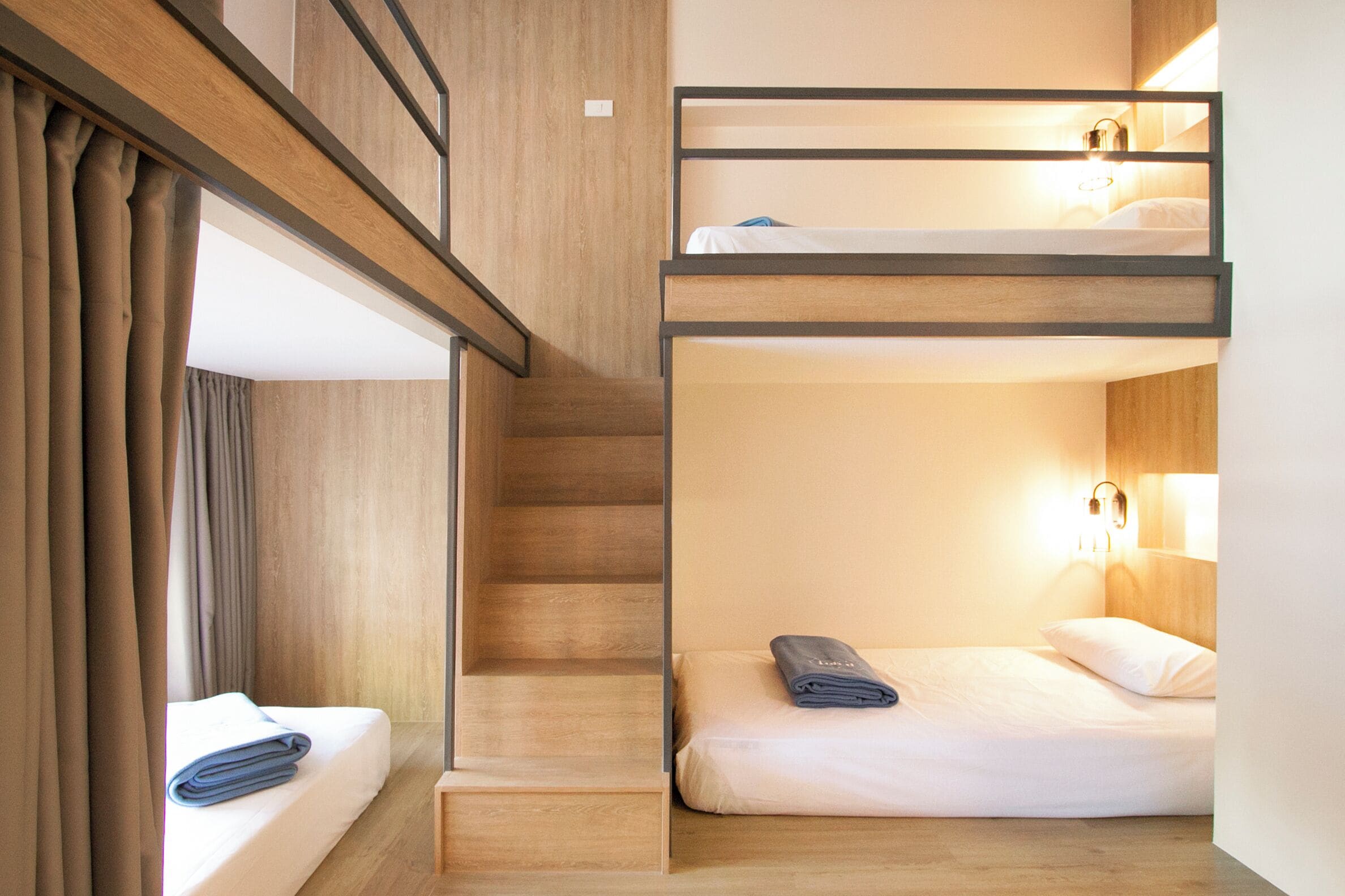 A bunk bed room with a wooden staircase and a single bed with a rolled towel.