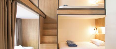 A bunk bed room with a wooden staircase and a single bed with a rolled towel.