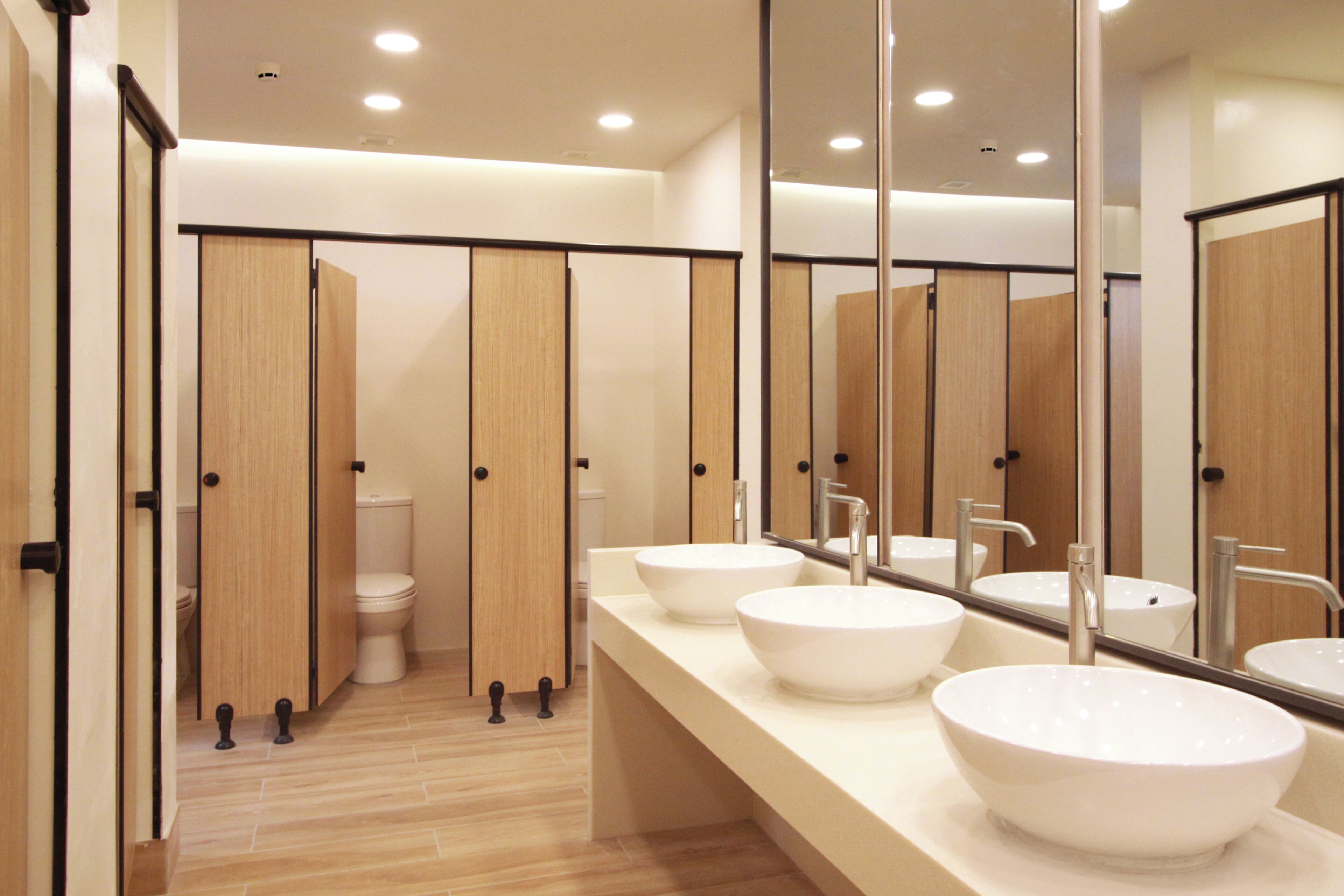 A modern bathroom with three sinks, a toilet, and wooden privacy partitions.