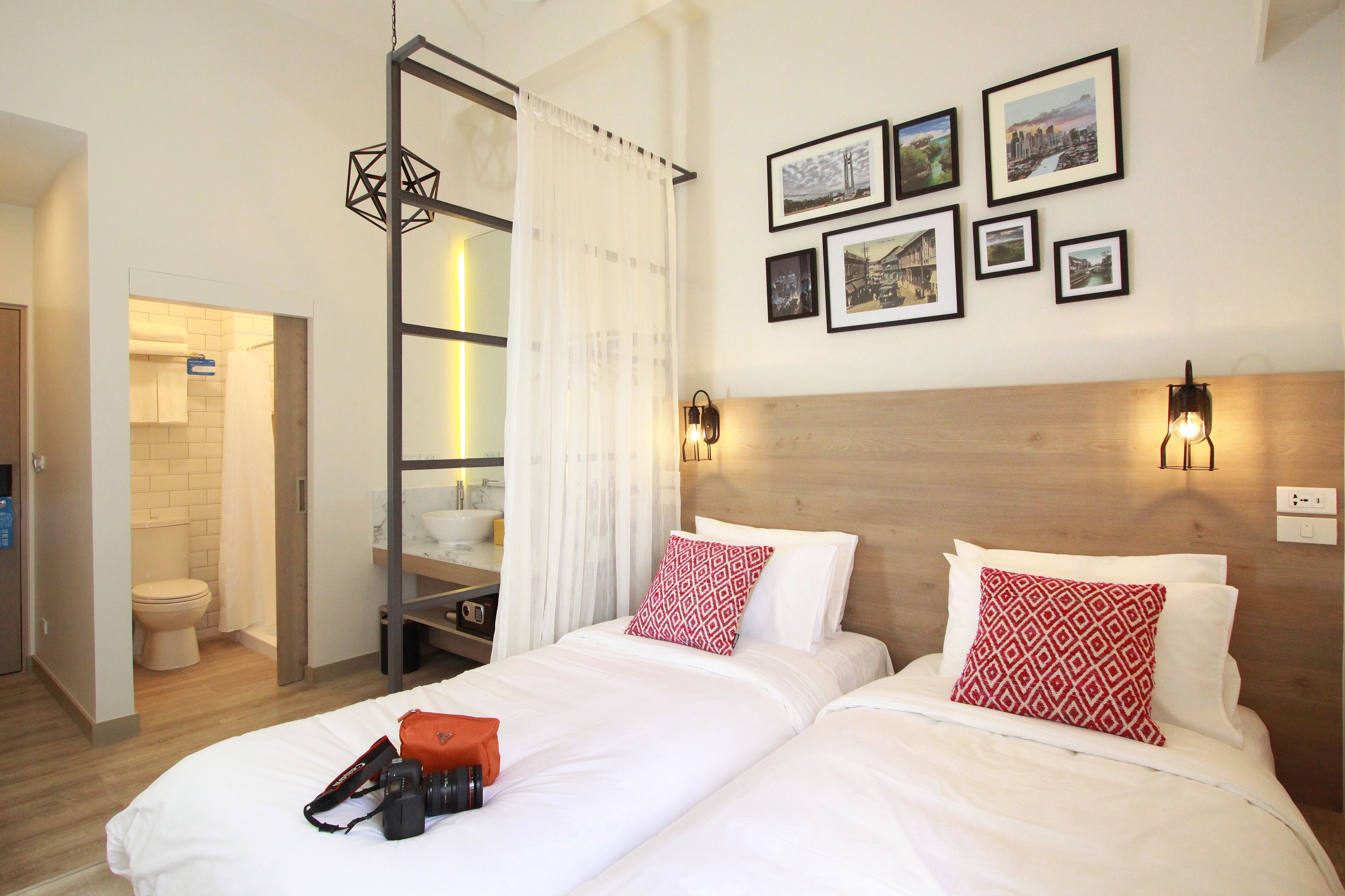 A hotel room with two beds, a wooden headboard, a wall-mounted light fixture, and a series of framed pictures.