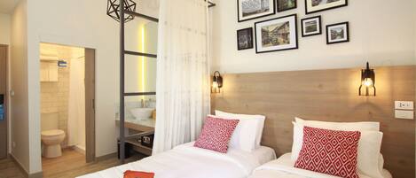 A hotel room with two beds, a wooden headboard, a wall-mounted light fixture, and a series of framed pictures.