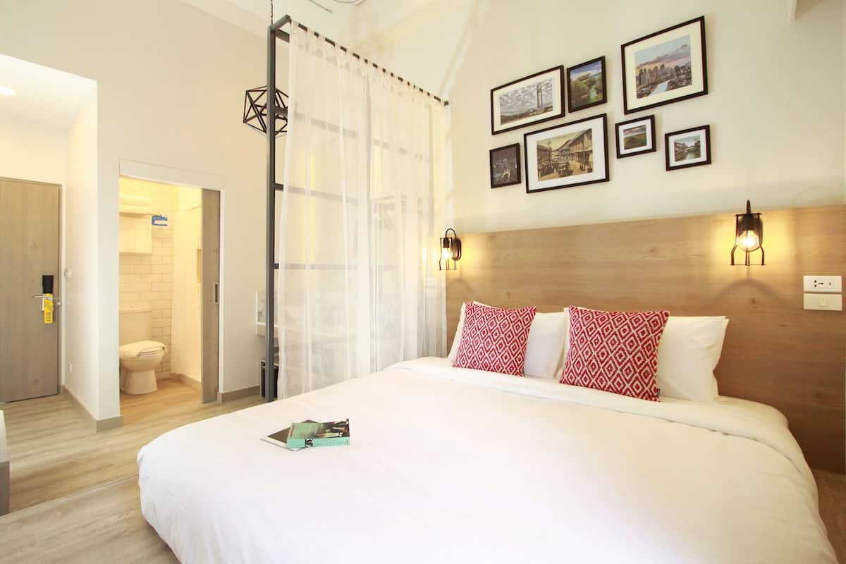 Quarto de hotel com uma cama grande, cabeceira de madeira e uma parede com quadros.