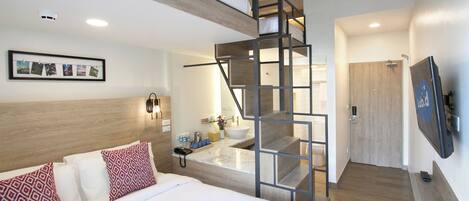 Una habitación de hotel moderna con una cama, un baño con lavamanos y una escalera.