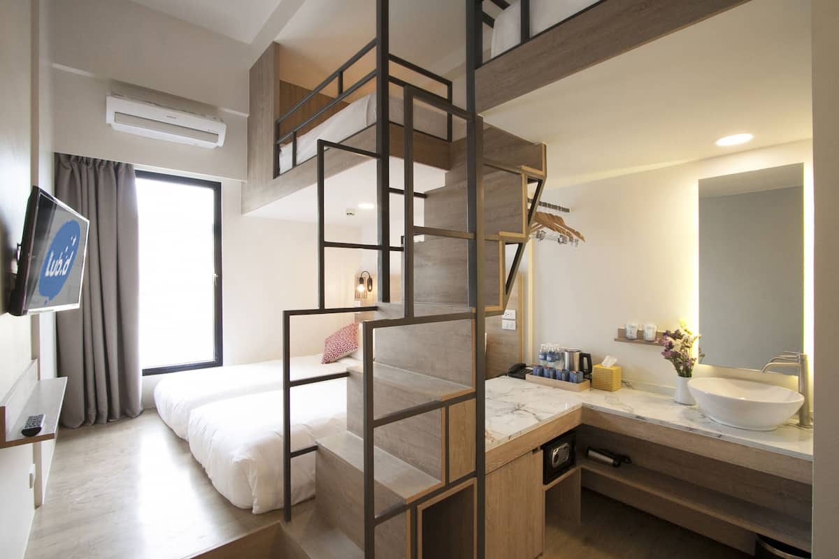 Quarto de hotel moderno com beliche, banheiro com um espelho grande e escrivaninha com televisão.