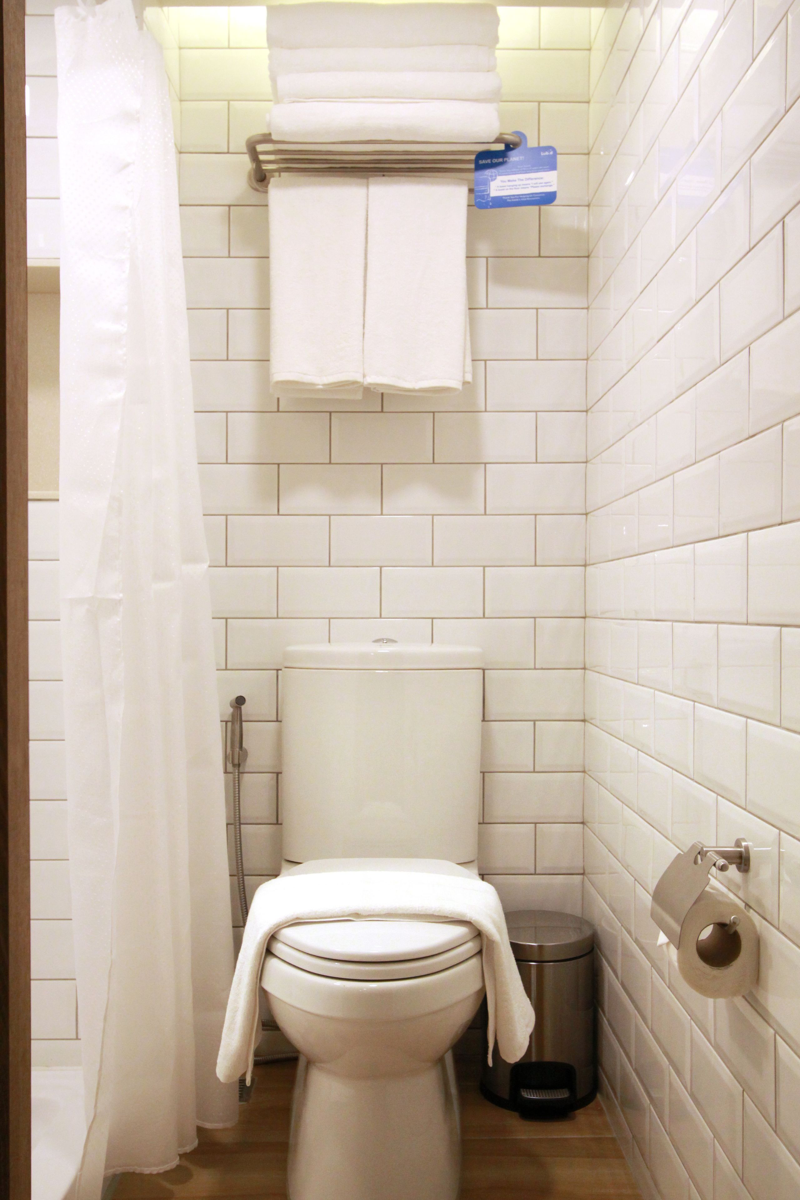 A small, clean bathroom with white tiles, a toilet, a shower, and a towel rack.