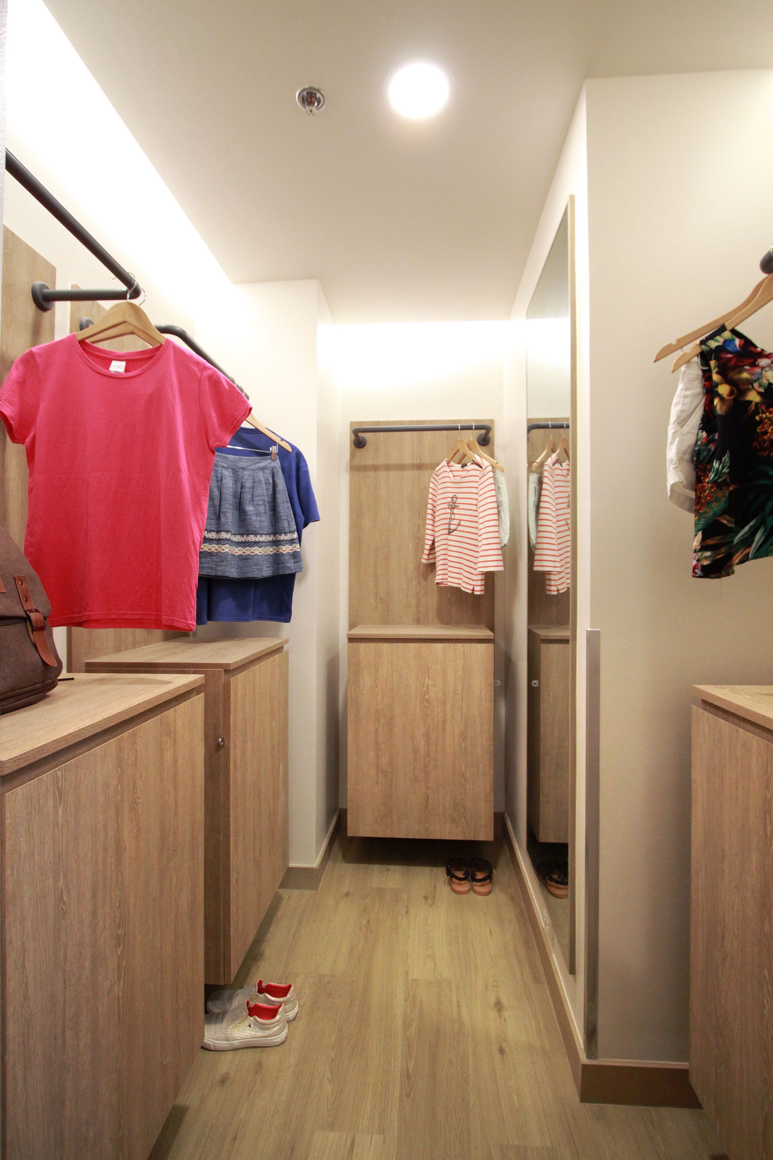 A narrow hallway with wooden cabinets, a mirror, and a hanging rack with clothes.