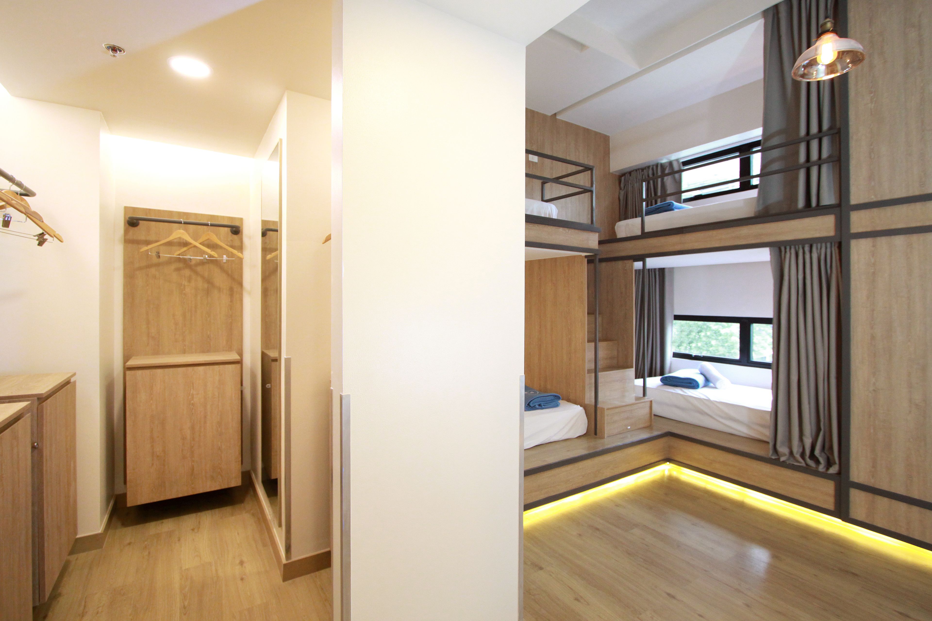 Una habitación de hotel moderna con una cama litera, suelo de madera, vestidor y ventana con cortinas.