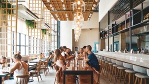 A spacious restaurant with high ceilings, wooden beams, and a long bar area.