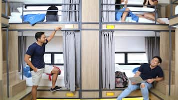 A multi-level bunk bed room with a wooden floor, a window, and a visible backpack on the top bunk.