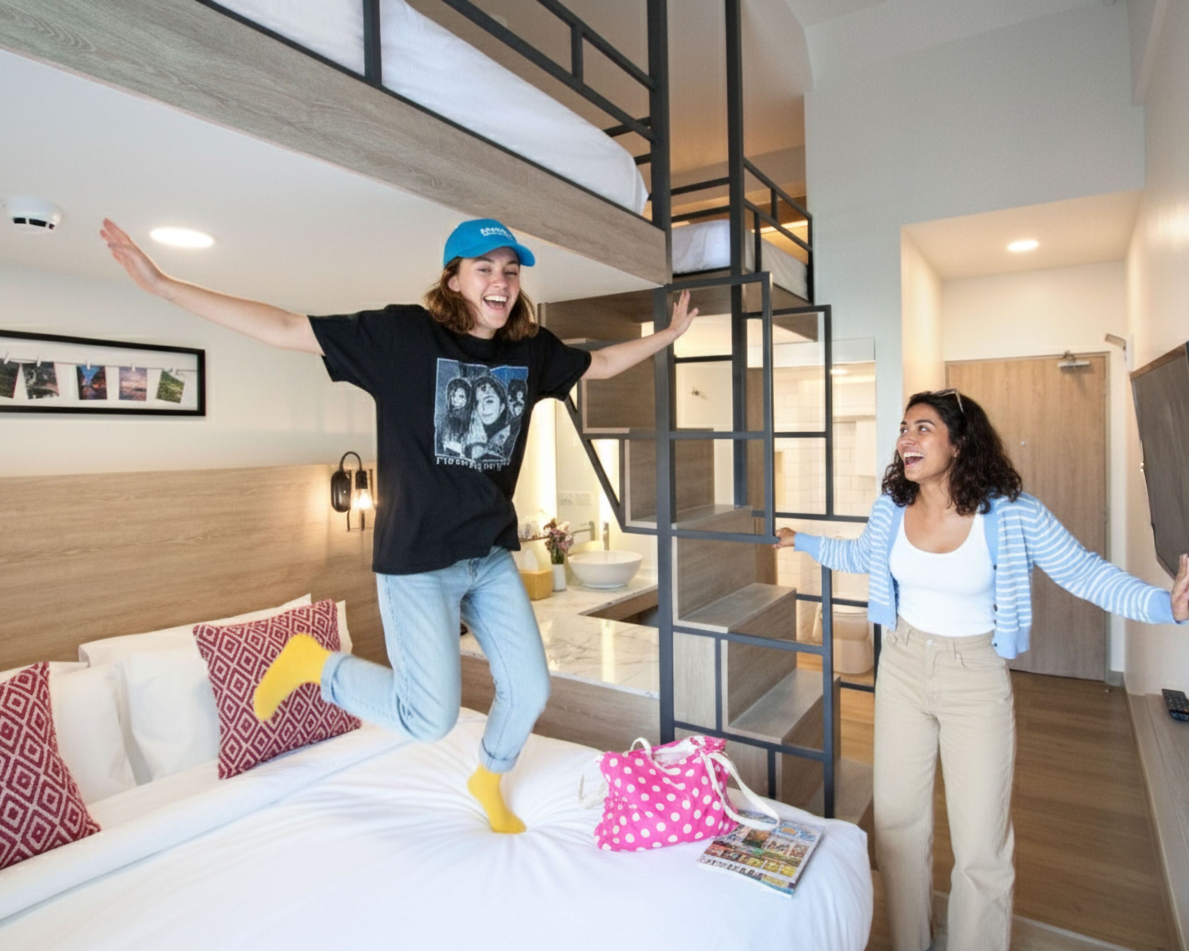 A modern hotel room with a bunk bed, a staircase, and a bathroom visible in the background.