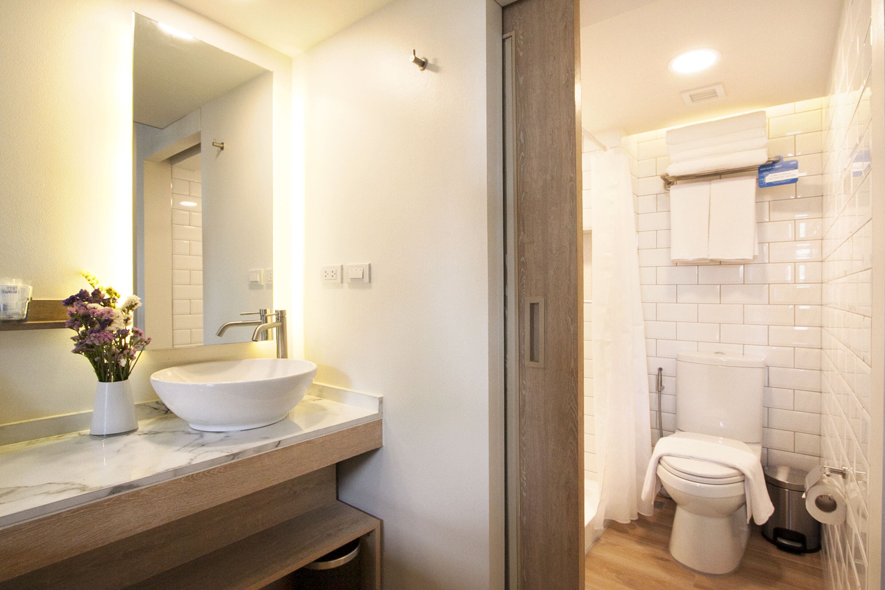 A modern bathroom with a large mirror, a white sink, a toilet, and a shower area.