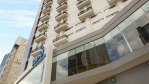 A multi-story hotel with a modern design, featuring balconies on each floor and a prominent entrance with glass doors.