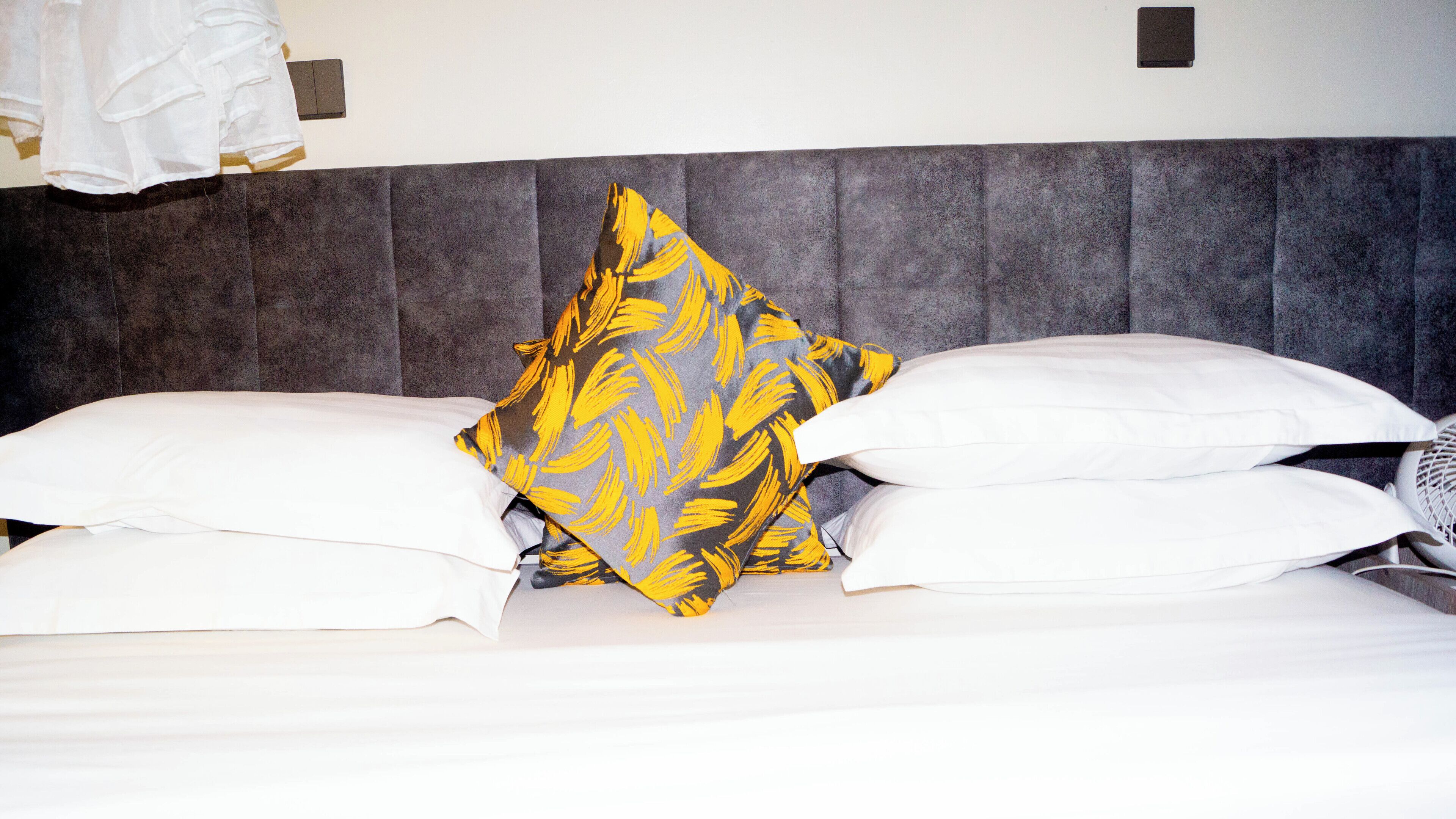 Una cama con almohadas blancas y una almohada decorativa con un diseño amarillo.