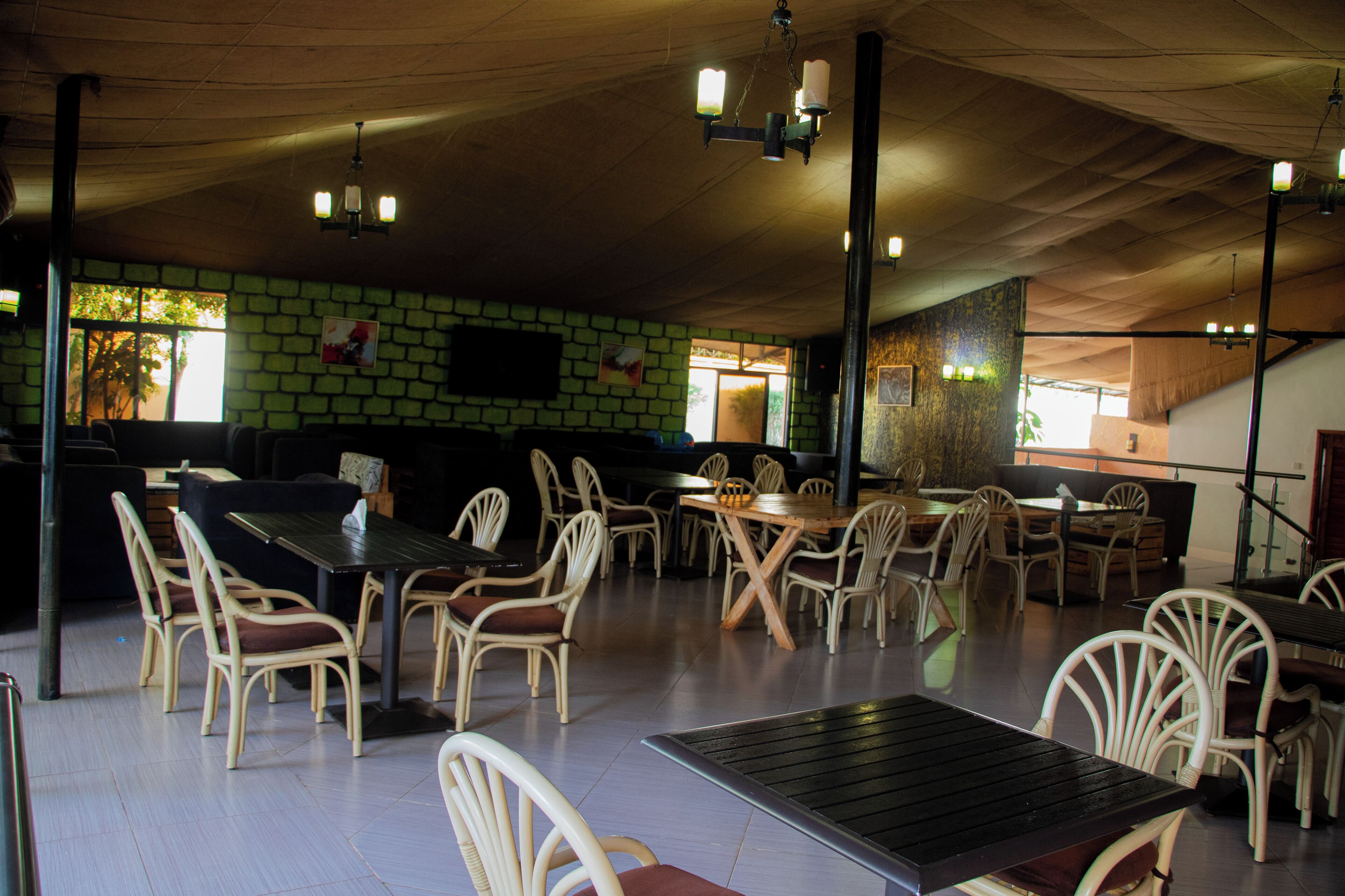Un restaurante con techos altos, mobiliario de mimbre y una pared de ladrillo verde.