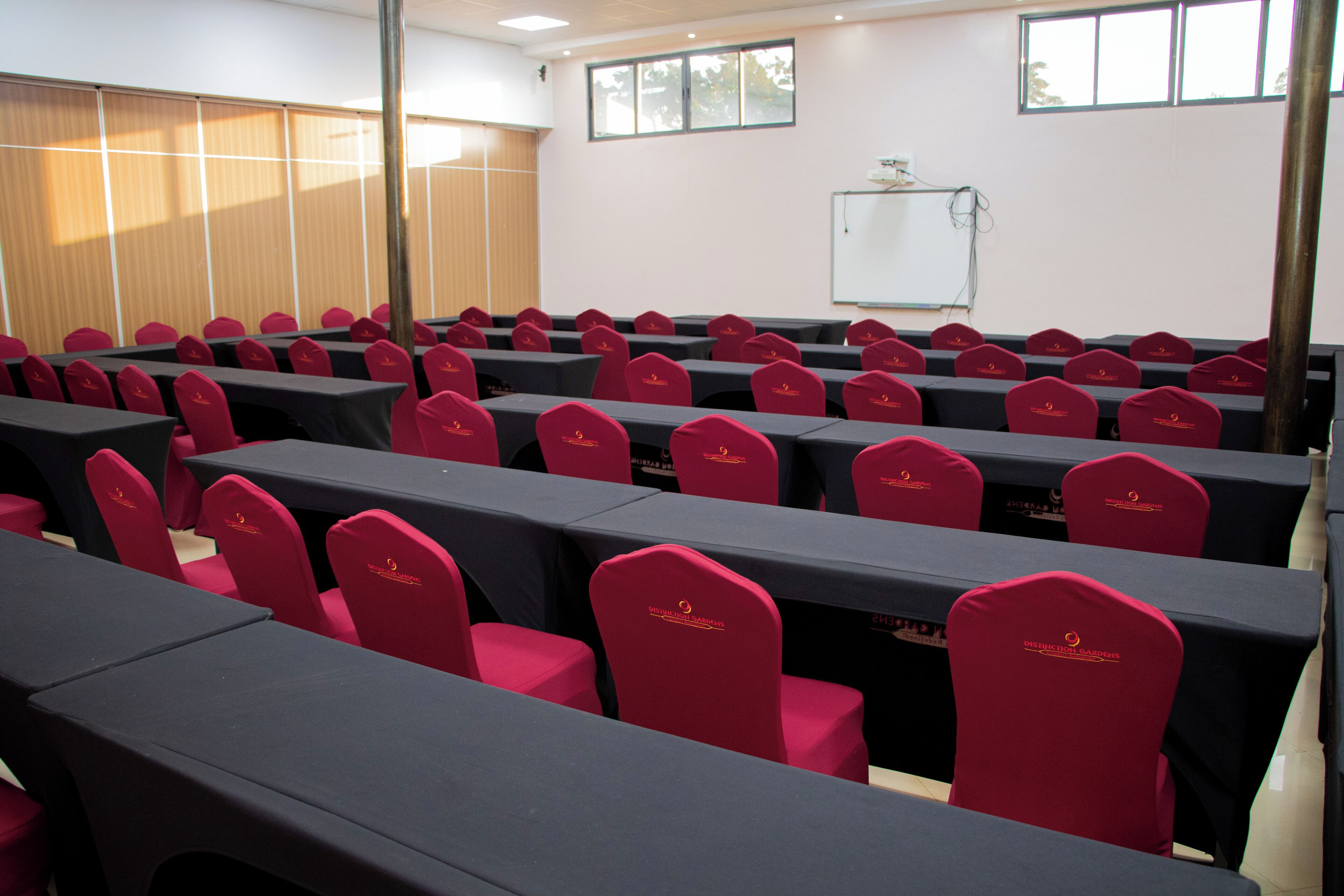 A conference room with rows of tables and chairs, a whiteboard, and a window with blinds.