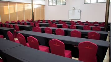 A conference room with rows of tables and chairs, a whiteboard, and a window with blinds.