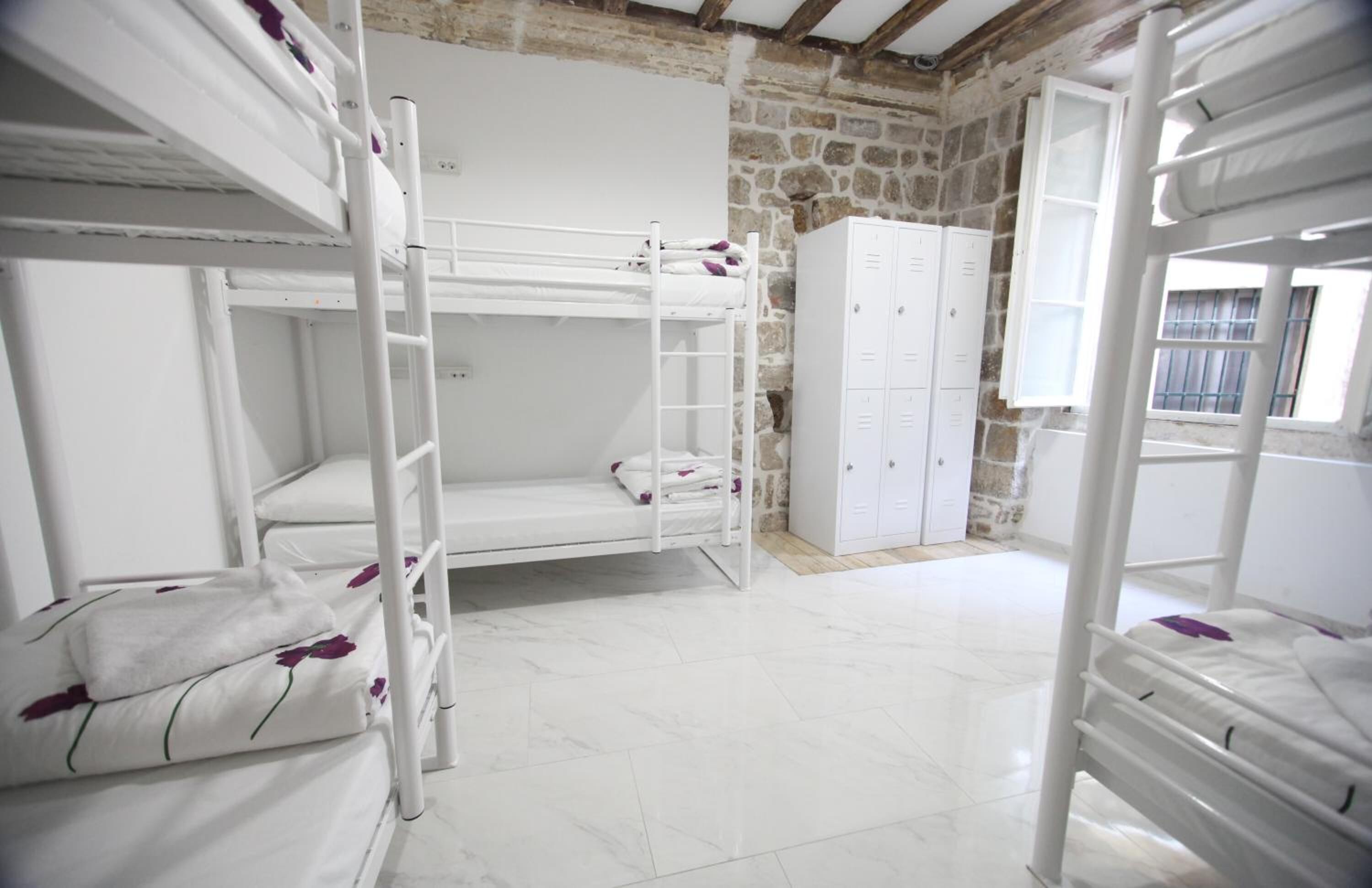 A dormitory room with bunk beds, a wardrobe, and a stone wall.
