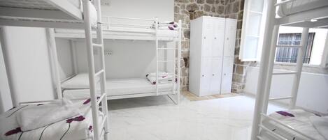 A dormitory room with bunk beds, a wardrobe, and a stone wall.