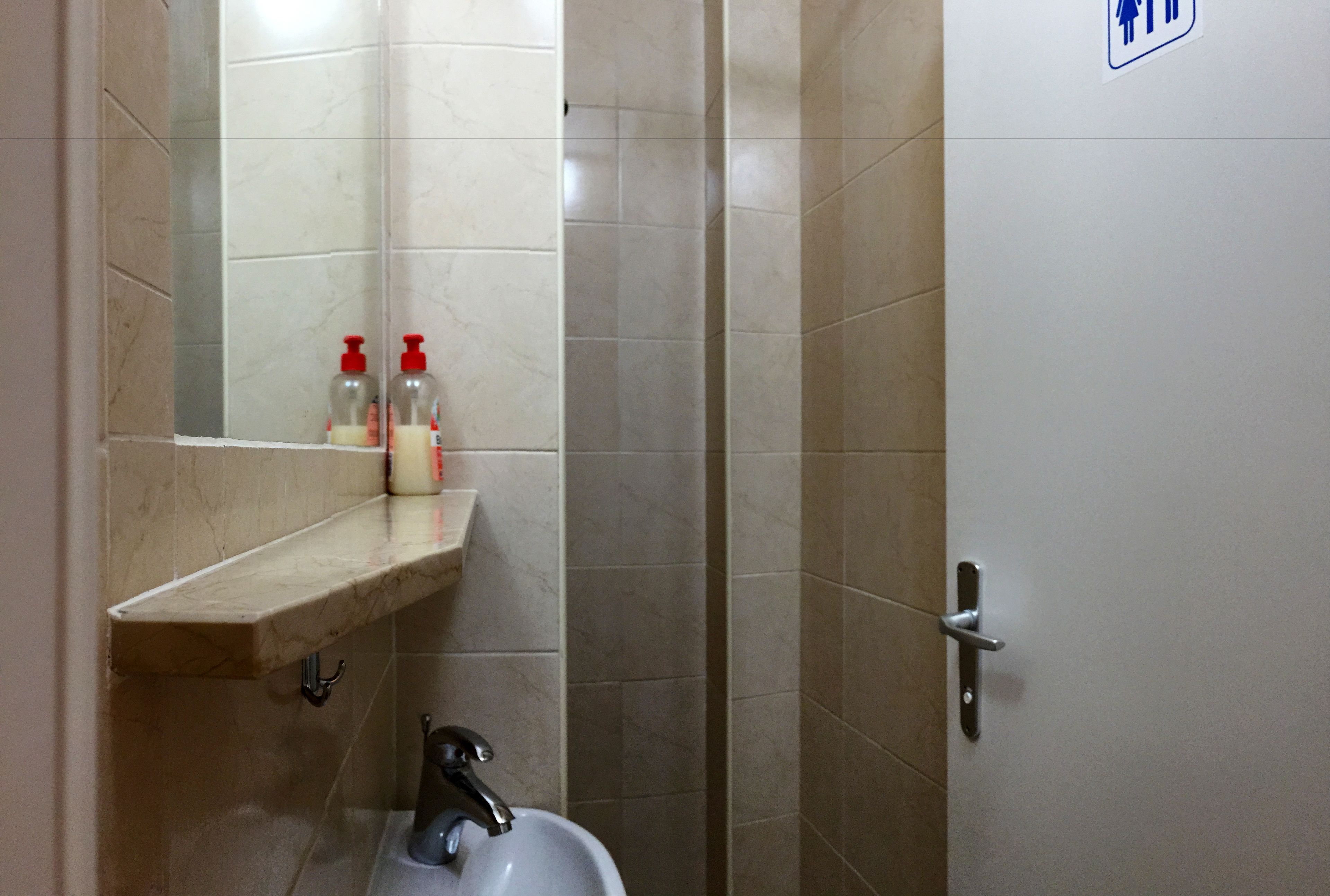A bathroom with a marble sink, a mirror, and a shelf with toiletries.