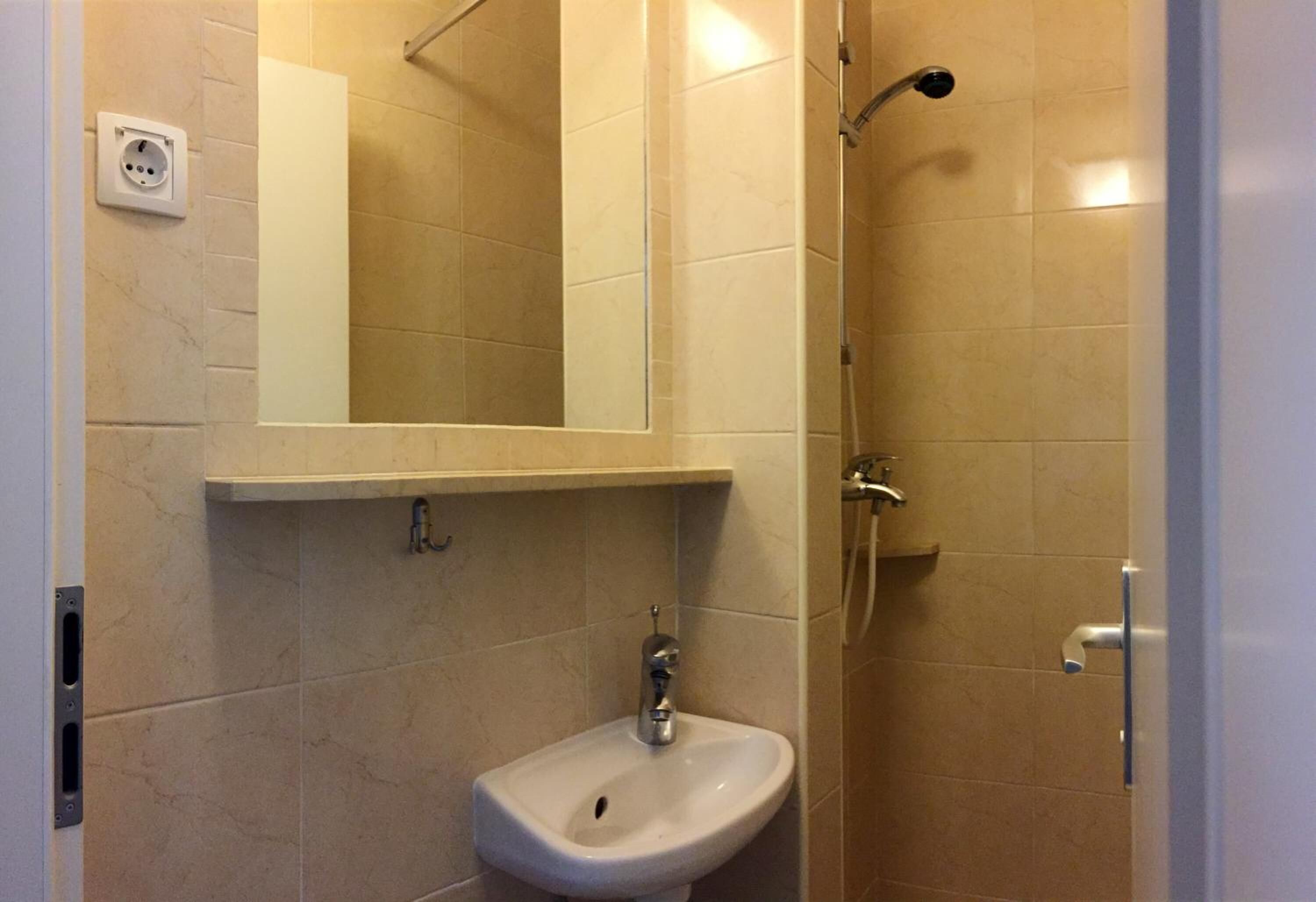 A bathroom with beige tiles, a white sink, a mirror, and a shower.