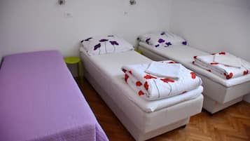 Una habitación con dos camas individuales, una mesita pequeña y un sofá morado.