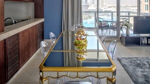 Un espace repas moderne avec une table à plateau en verre, des chaises transparentes et un centre de table composé de fruits.