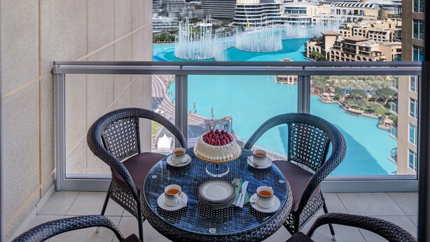 Un balcon avec une table dressée pour deux personnes, offrant une vue sur le paysage urbain et un point d’eau.
