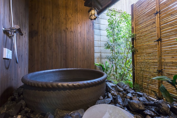 Un baño al estilo japonés tradicional con una gran bañera de piedra caliente, paredes de madera y una cerca de bambú.