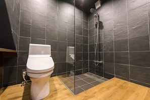 Un baño moderno con inodoro blanco, ducha con cerramiento de vidrio y paredes cubiertas de baldosas oscuras.