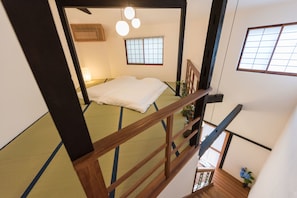 Una habitación tradicional japonesa con suelo de tatami, una cama baja y una escalera de madera.
