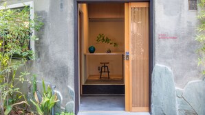 Una entrada japonesa tradicional con un puertas correderas, un pequeño taburete y un estante con una planta y un objeto decorativo.
