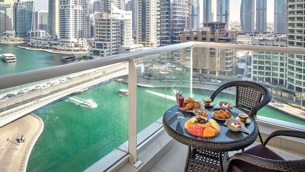 A balcony with a table set for breakfast, overlooking a marina and a city skyline. - Luxury Staycation - Continental Tower (Dubai)