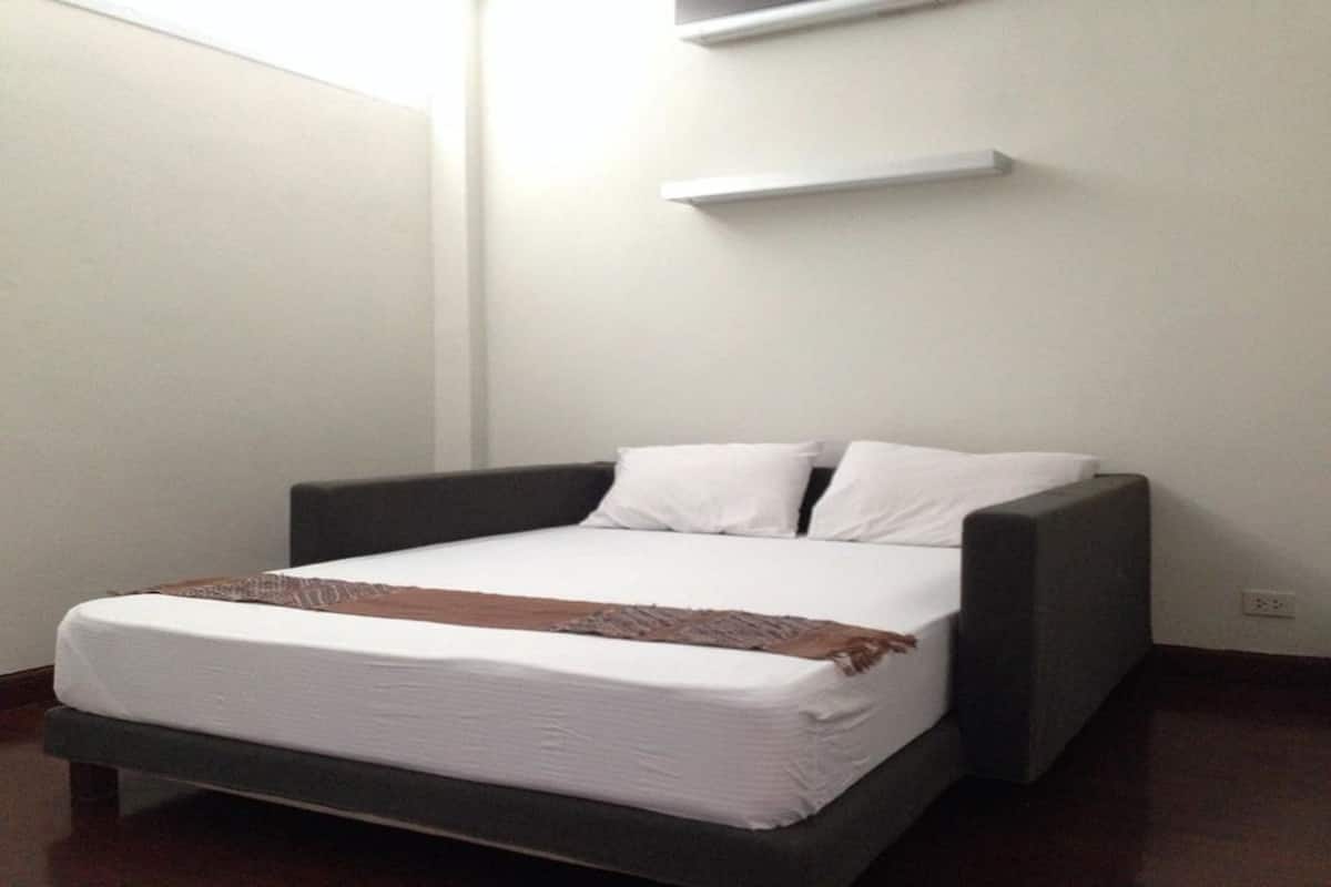 A single bed with a dark headboard, white bedding, and a brown throw blanket.