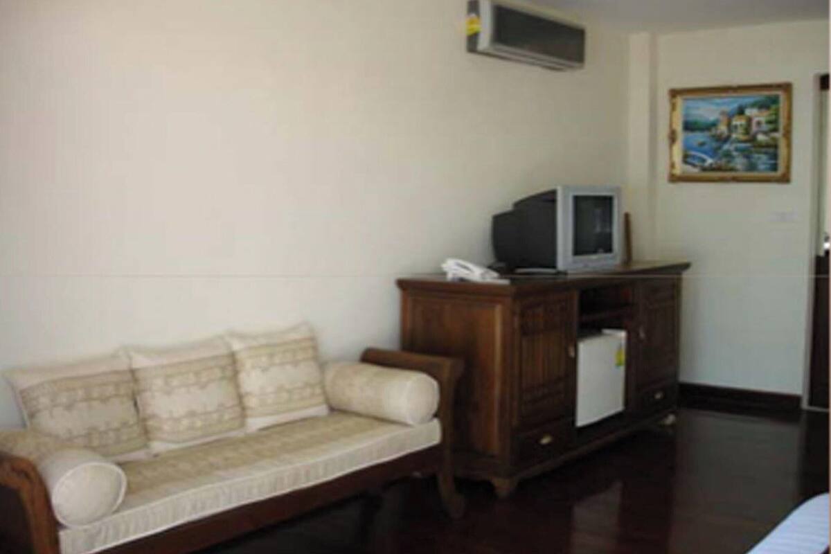 A room with a wooden sofa, a small cabinet with a television, and a painting on the wall.